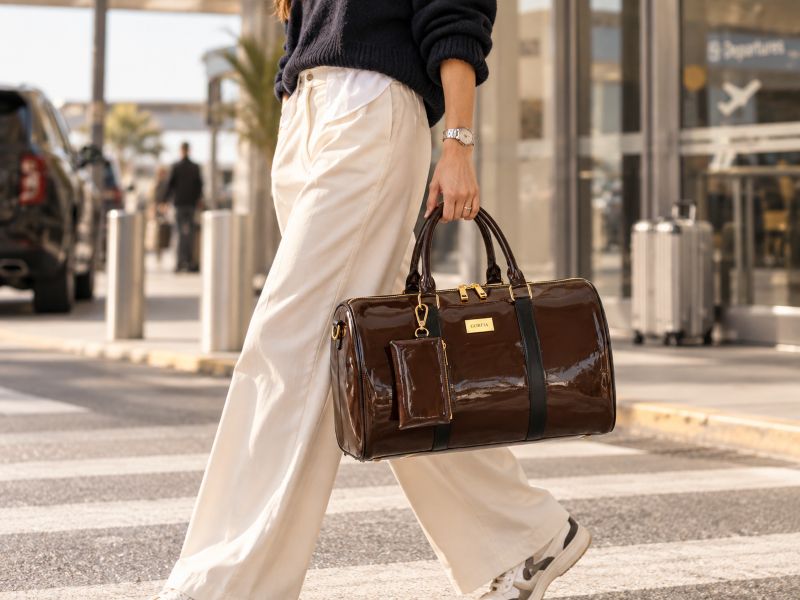 woman‑carrying‑glossy‑brown‑patent‑leather‑weekend‑duffle‑bag